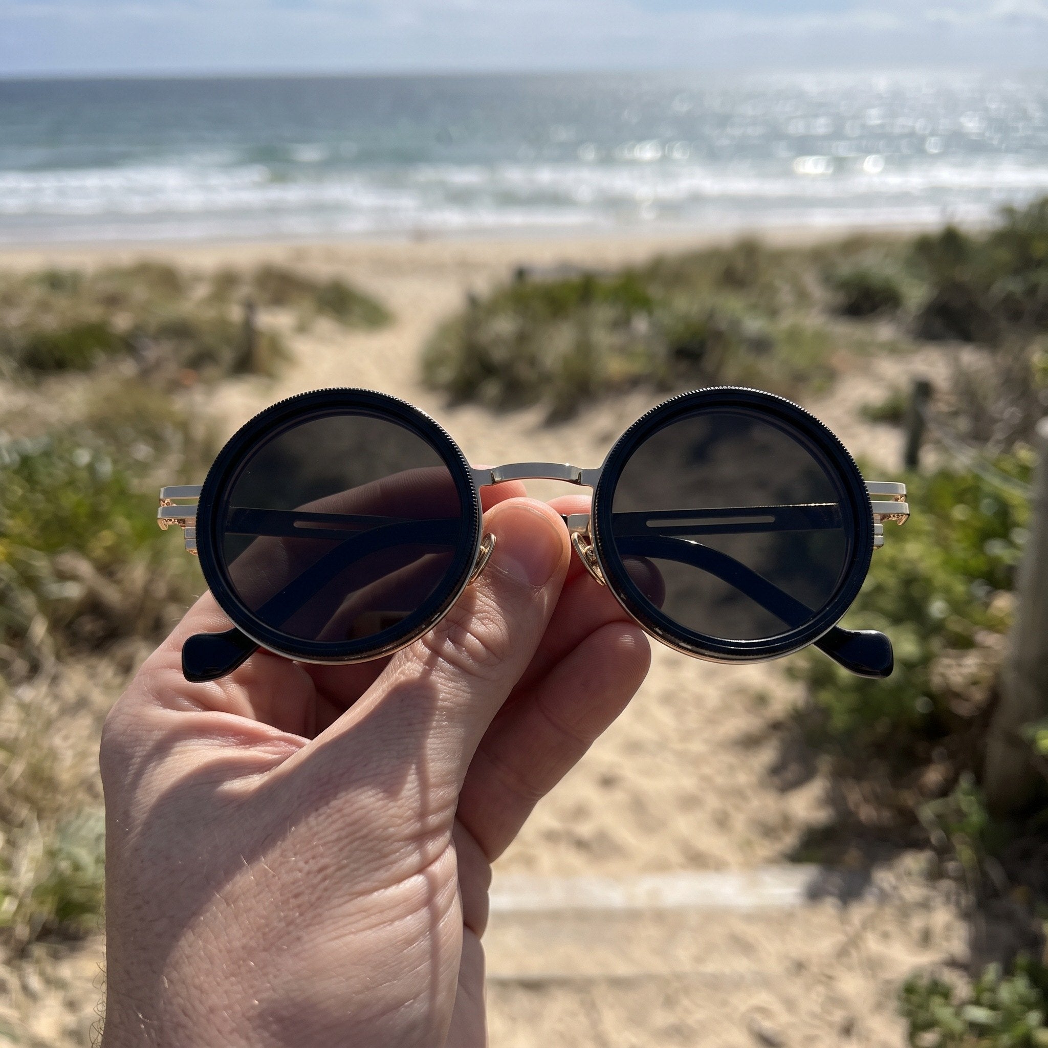 Gold sunglasses held before a sunny beach walk
